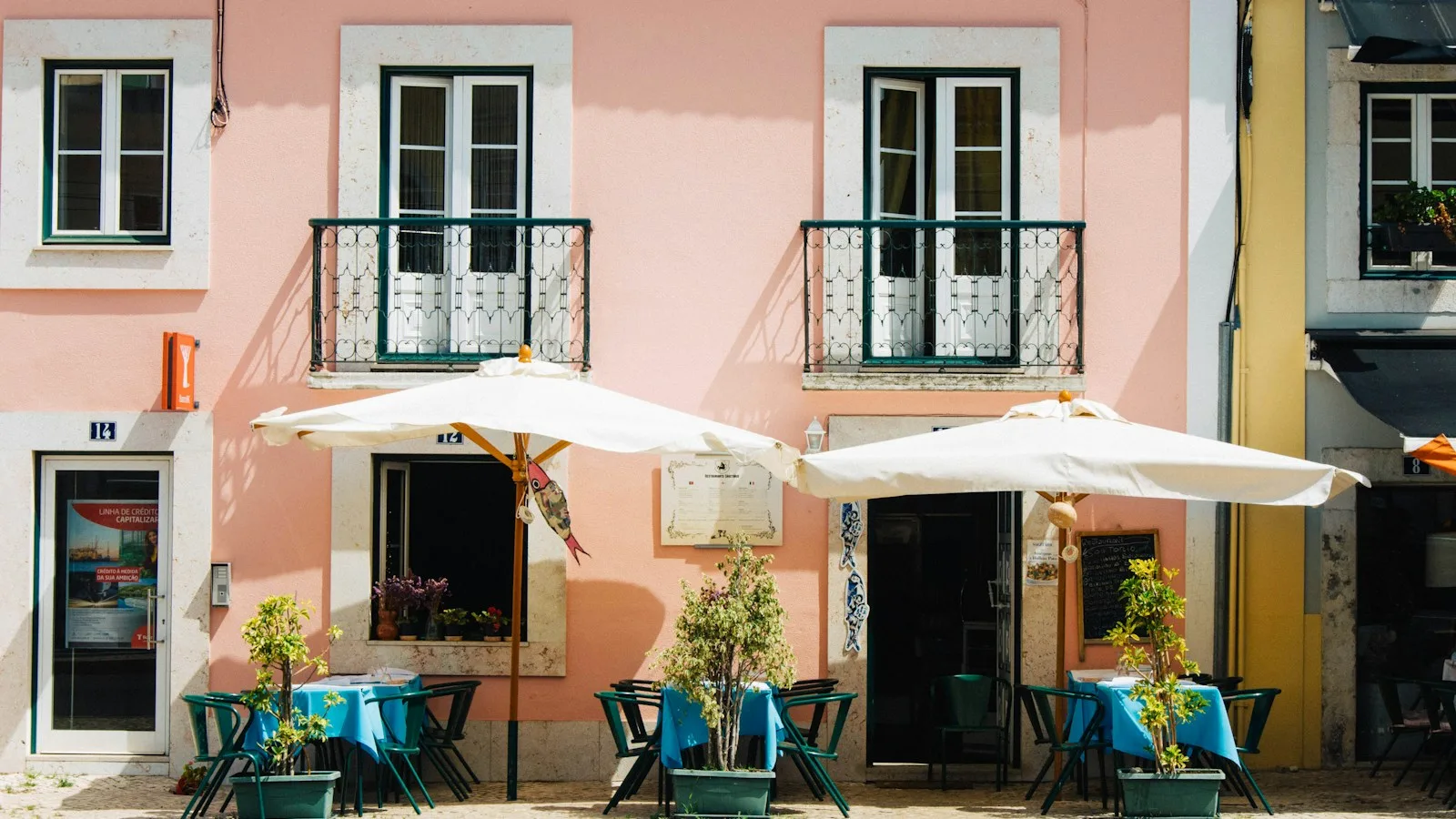 Terrasse de restaurant avec parasols devant une façade rose typique de Lisbonne